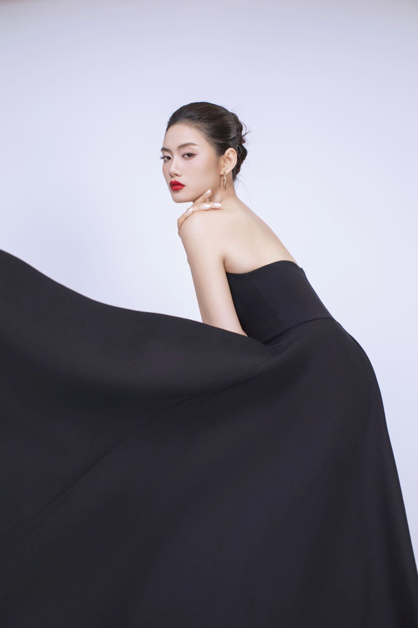 Woman in a black strapless dress with a flowing fabric against a white background