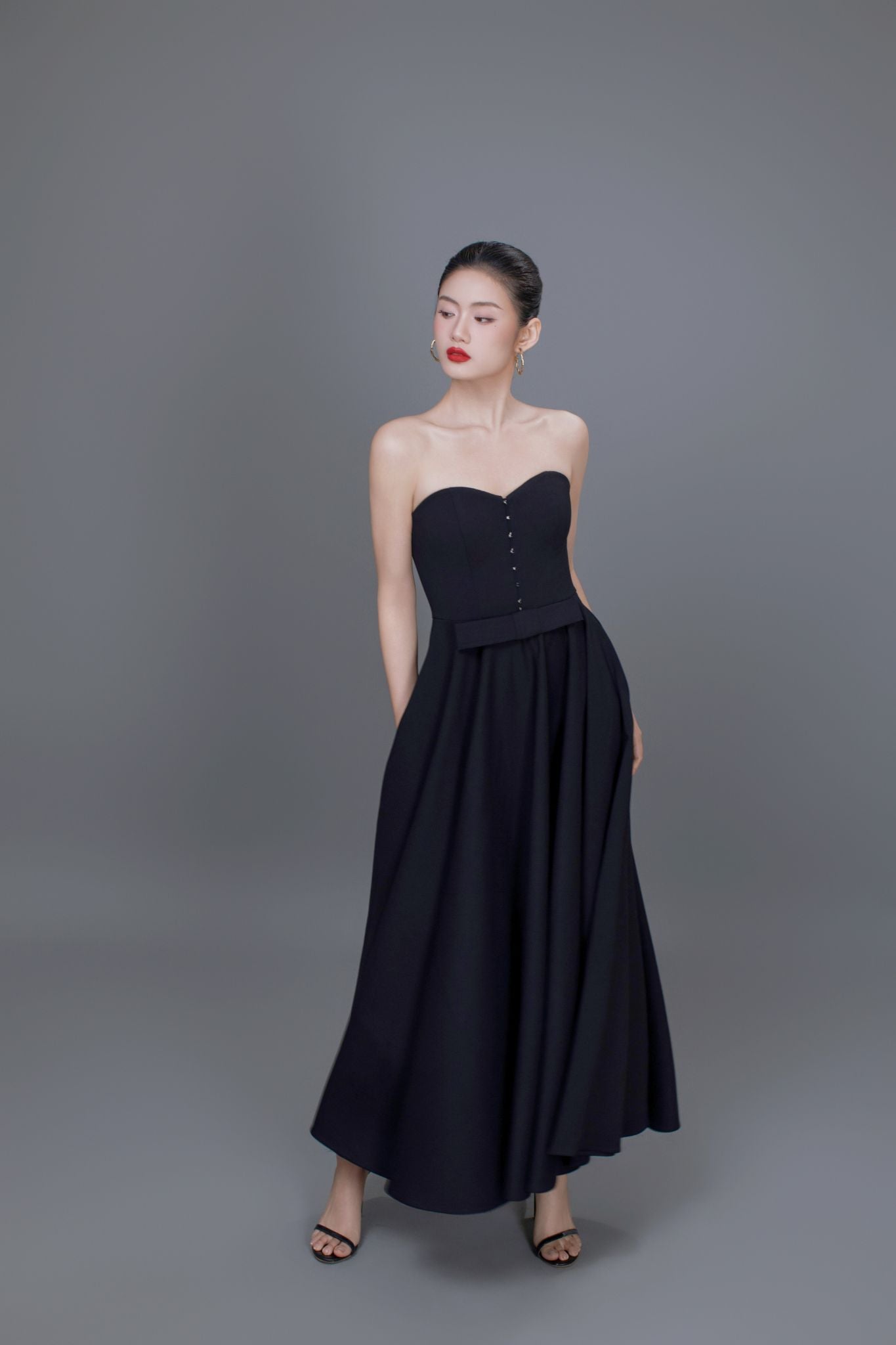 Woman wearing a black strapless dress against a gray background