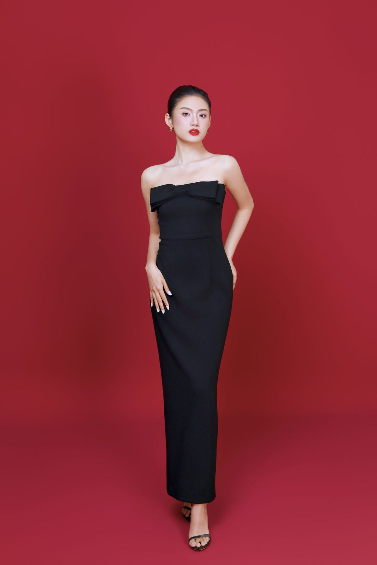 Woman wearing a black strapless gown against a red background