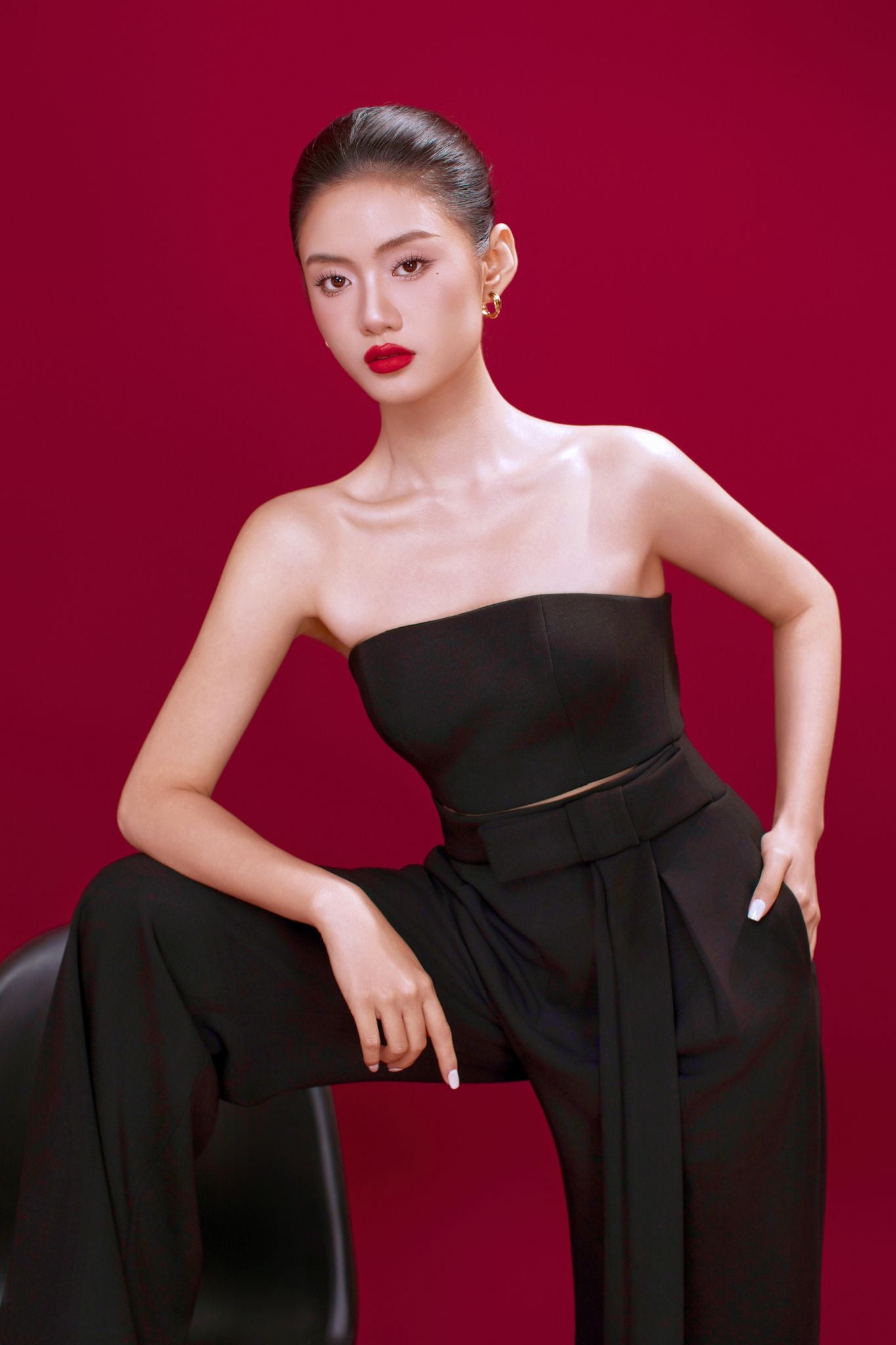 Woman in a black strapless top and pants against a red background