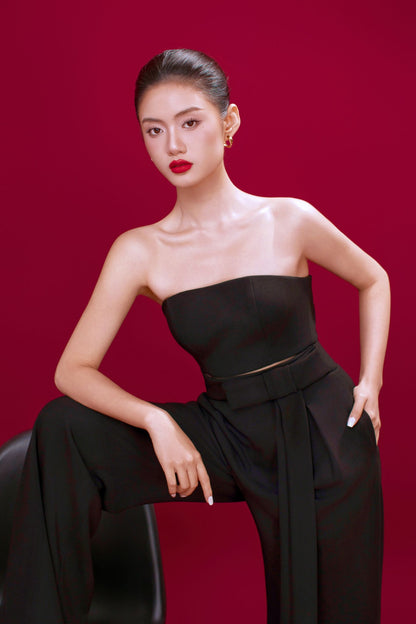 Woman in a black strapless top and pants against a red background