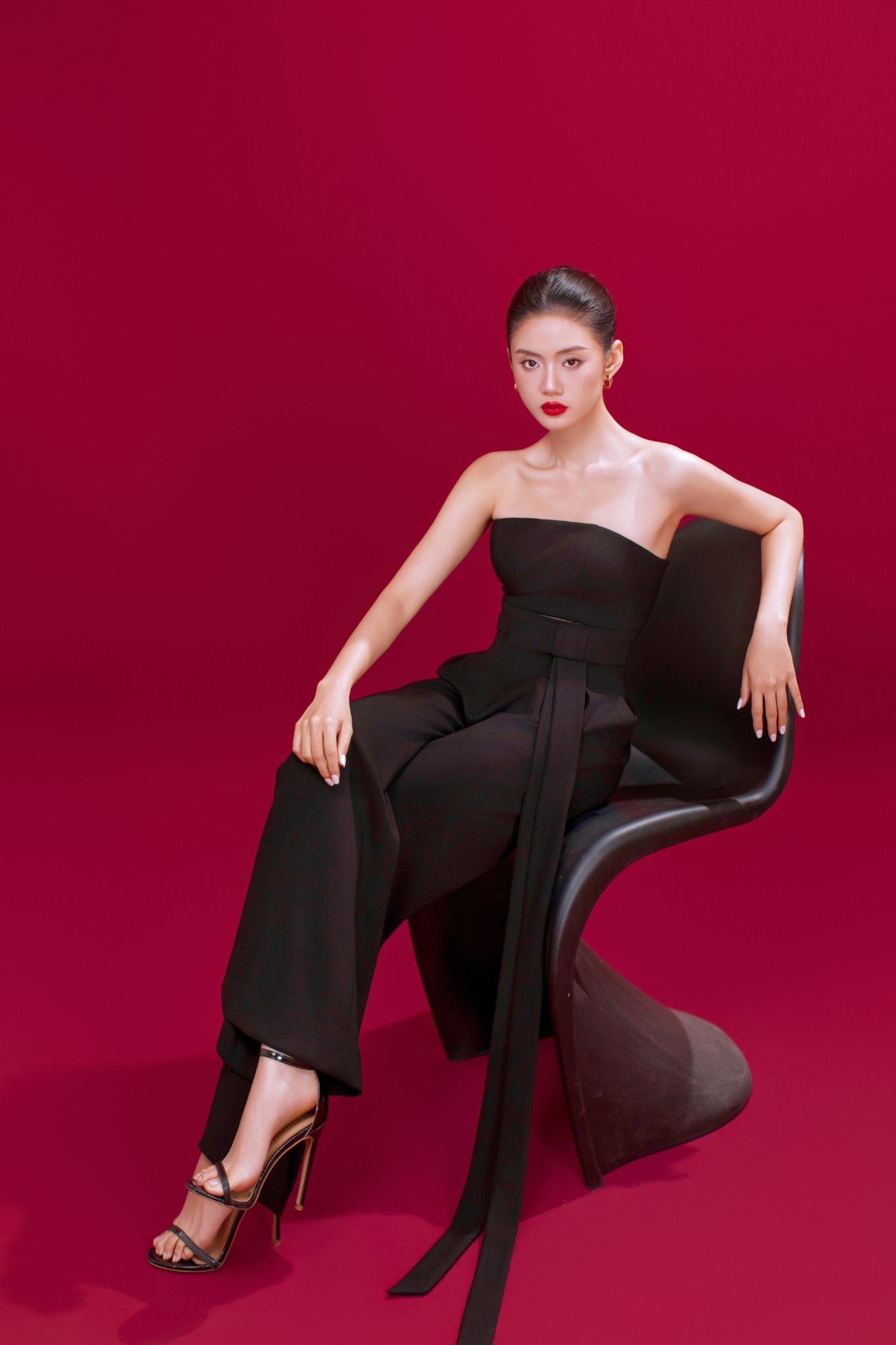 Woman in a black outfit sitting on a chair against a red background