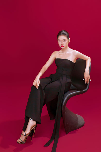 Woman in a black outfit sitting on a chair against a red background